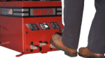 Operator pressing the foot pedals on a Coats RC-series tire changer, showing the red control panel with clamp and rotation icons and the machine’s lower chassis